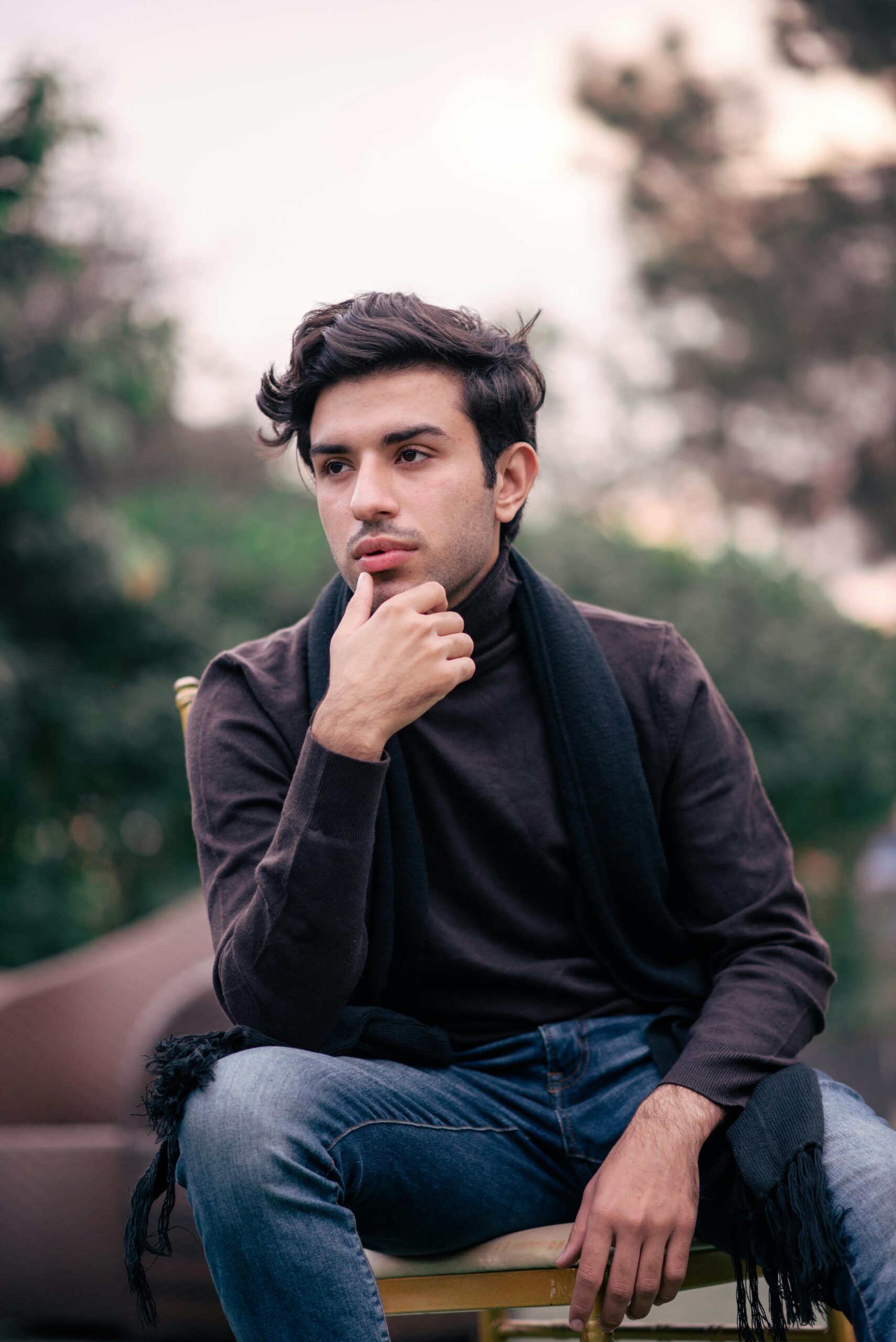 Portrait of a young man sitting outdoors in Sialkot, Pakistan, wearing denim and a scarf.